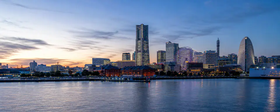 Illustrated panorama of Yokohama's waterfront with skyscrapers, a Ferris wheel, red-brick warehouses, and reflections in evening light
