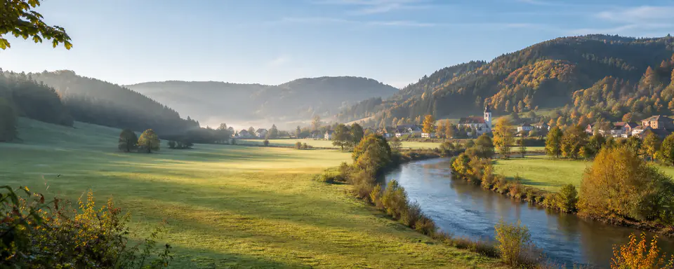 Illustrated German landscape with a river valley, green meadows, and a village in autumn light